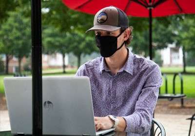 Max Riley sitting outside working on laptop wearing a mask