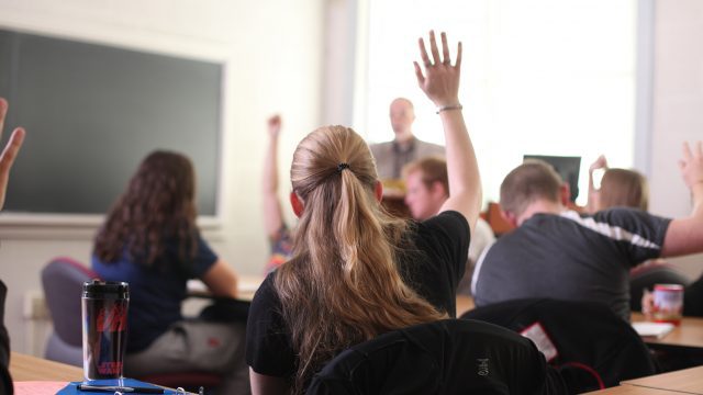 The back of students' heads raising their hands in class