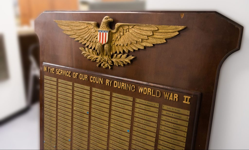 A large wooden board with a gold Eagle on top and the words "In Service of our country during World War II." A list of names is shown underneath