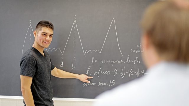 Student pointing at chalkboard with math equation on it