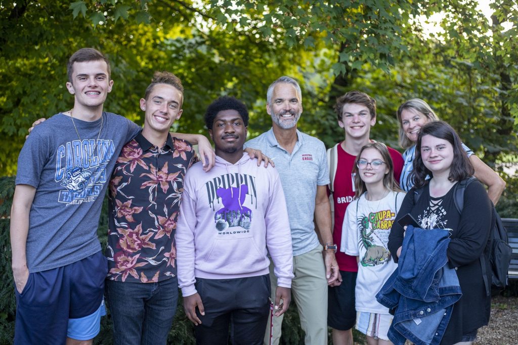 Six students pose for a photo outside with Bridgewater College President David Bushman and his wife, Suzanne. All are smiling.