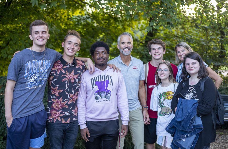 Six students pose for a photo outside with Bridgewater College President David Bushman and his wife, Suzanne. All are smiling.