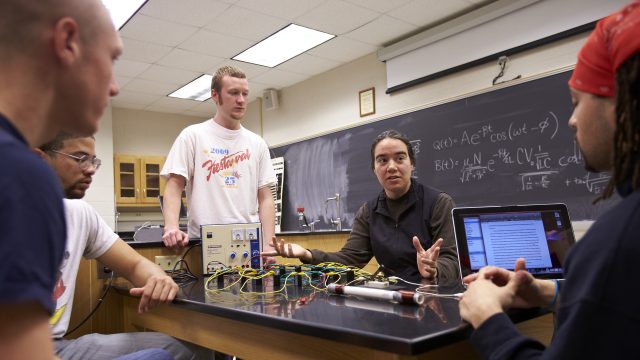 Professor sitting with students during physics class