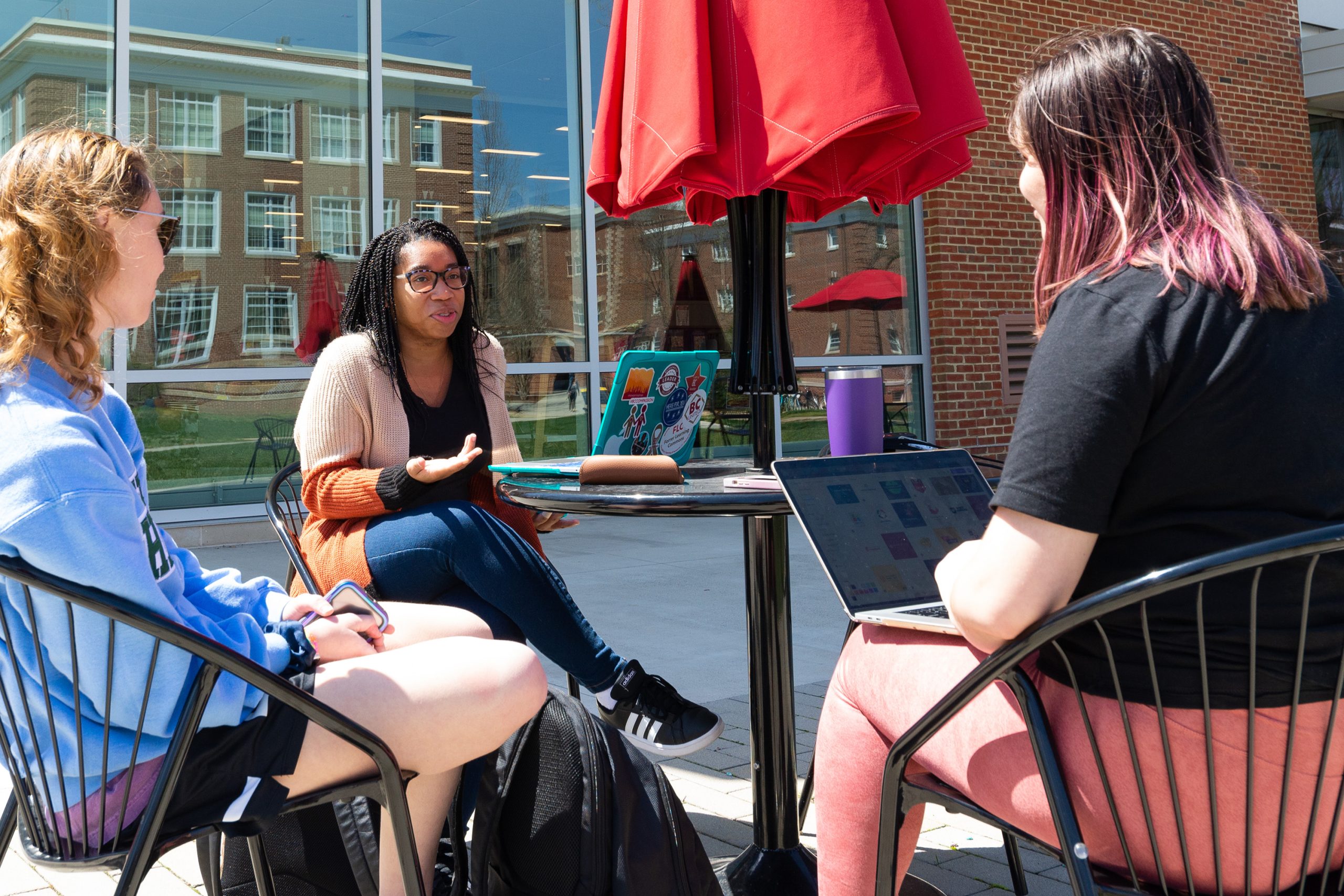 Students sitting at a table with an umbrella talking outside the Forrer Learning Commons