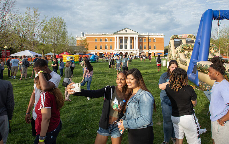 Students posing for a selfie during spring fest with McKinney Hall in the background surrounded by other students