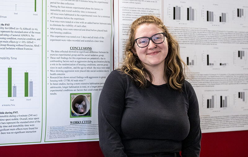 Student standing in front of presentation posters smiling