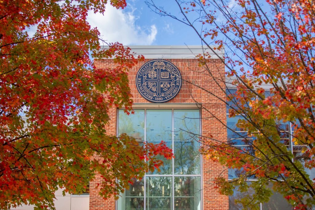The exterior of the Forrer Learning Commons that shows the Bridgewater College seal. Trees with fall leaves surround it.