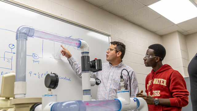 Engineering professor pointing to information on whiteboard with a student looking over his shoulder behind him