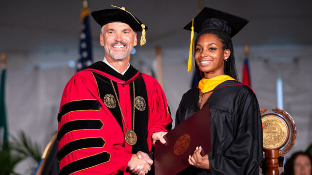 Dr. Bushman shaking student's hand after handing her her diploma at commencement