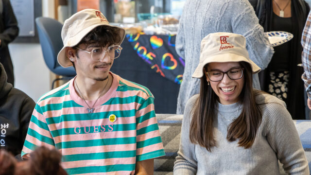 Two students with B-C floppy hats smiling sitting next to each other