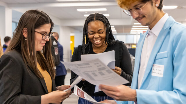 Three students gathered together with papers in hand