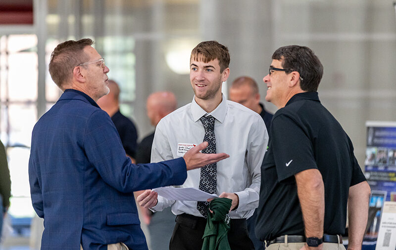 Business professor speaking with current student and local business owner at the career fair