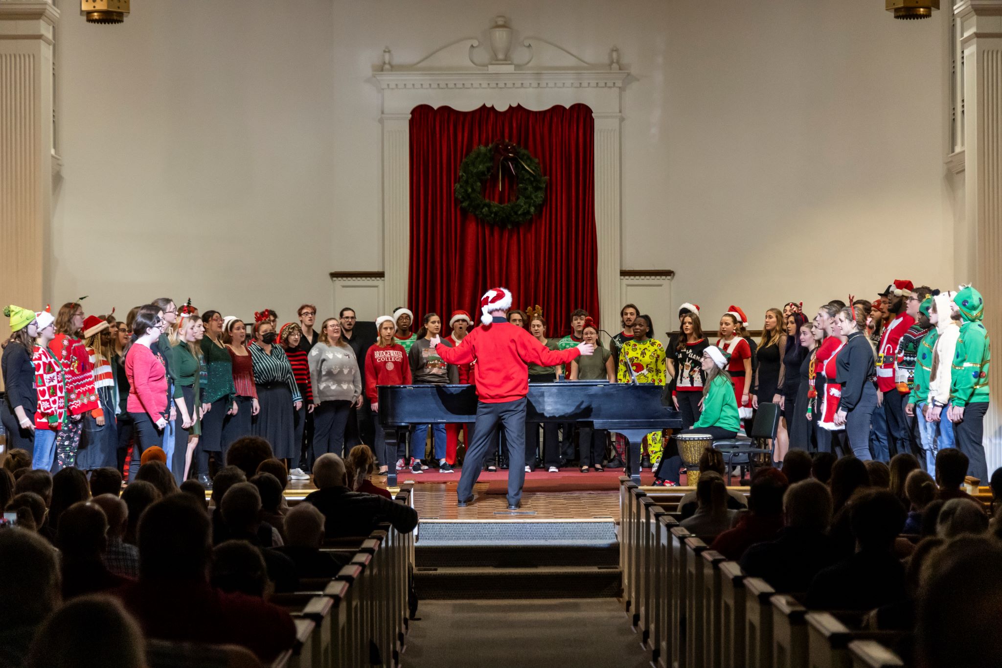 Choir singers dressed in holiday apparel perform on stage for an audience