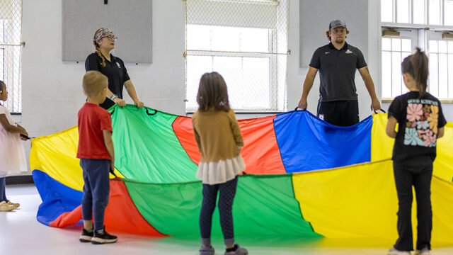 Students playing parrachute games with young children