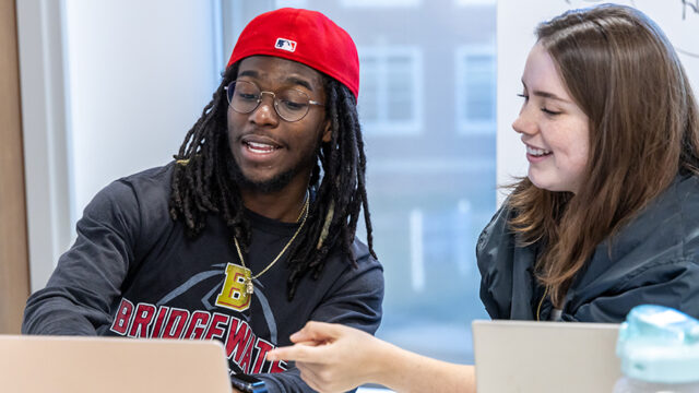 Students working together in class. One student is pointing to a laptop in front of them.