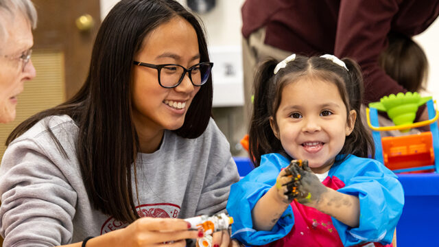 Female student smiling at young child who's hands are covered in black paint