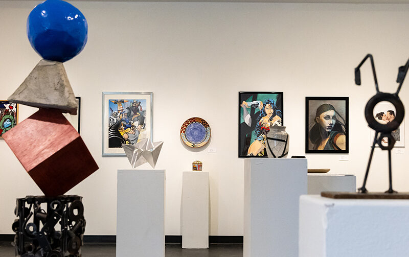 Art gallery with paintings on the back wall and sculptures scattered throughout the room in the foreground