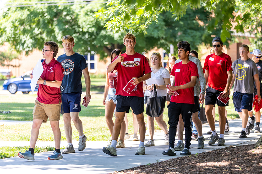 Line of students walking on campus during orientation. One student giving a thumbs and smiling for the camera.