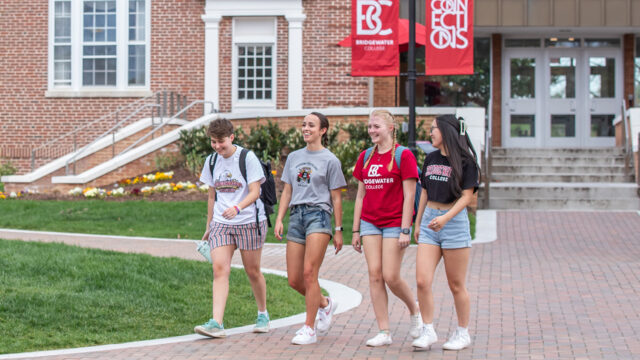 Four Bridgewater College students wearing B-C gear walking on a brick path on campus