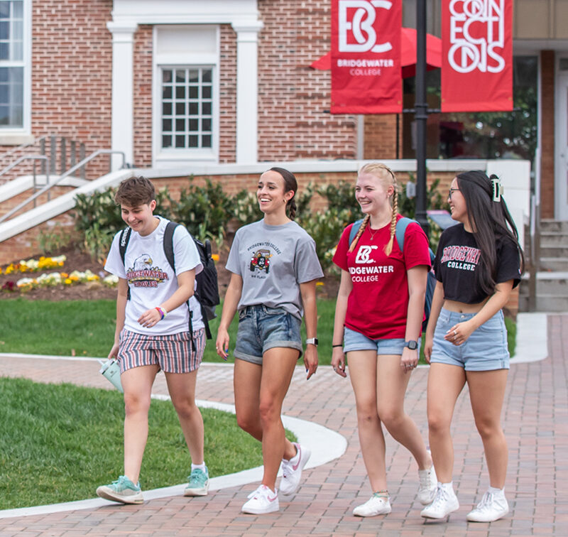 Four Bridgewater College students wearing B-C gear walking on a brick path on campus