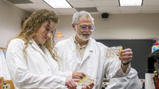 Dr. Baron and a Bridgewater College biology degree student collaborating on lab research in white lab coats.