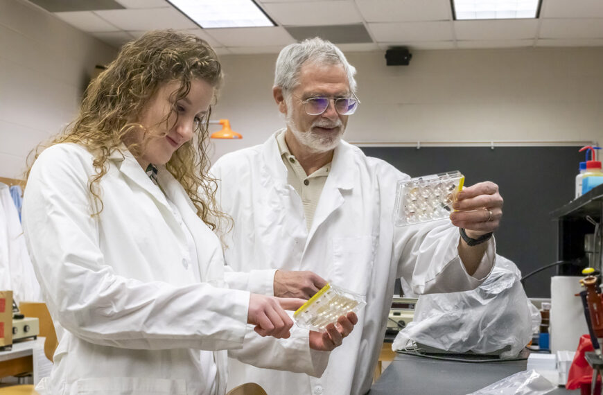 Dr. Baron and a Bridgewater College biology degree student collaborating on lab research in white lab coats.