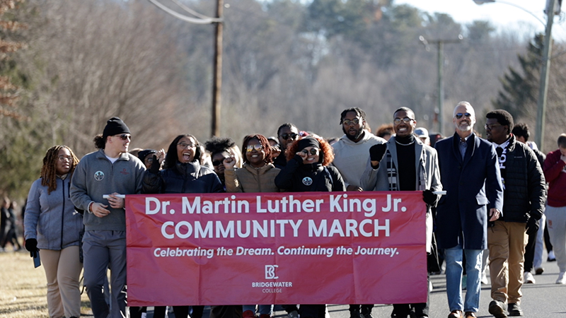 A group of predominantly black students smiling and carrying a sign that reads Dr. Martin Luthor King Jr. Community March