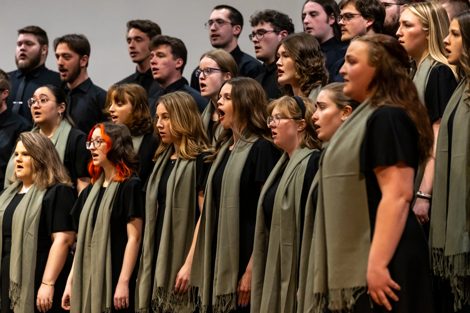 A choir of men and women singing in performance on risers.