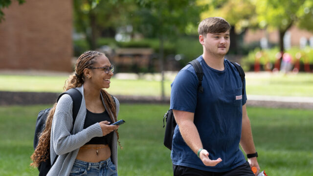 One student laughs at another as they walk together through the campus mall
