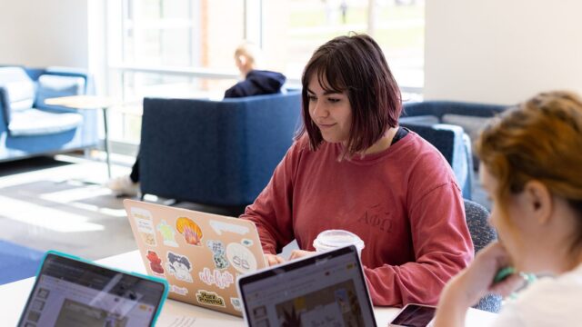 A student sits with a group and studies on her laptop